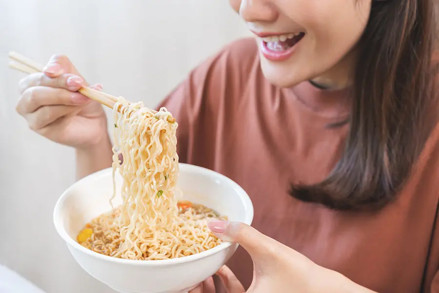 A woman lifting noodles from a bowl of chicken soup noodles