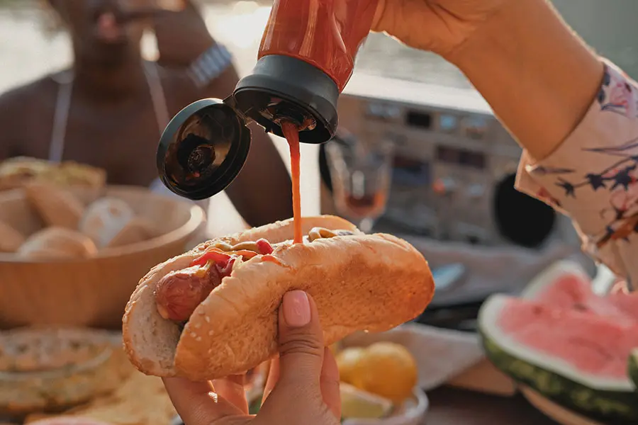 Pouring tomato sauce on a hot dog