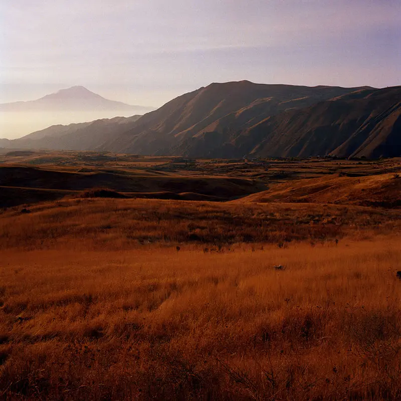 Vast, dry hills stretch across the landscape, bathed in warm golden tones, under a soft, hazy sky.