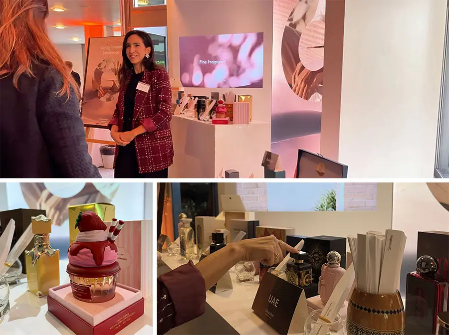 Danielle fragrances at the investor conference booth, with a digital screen behind her. The lower section showcases colourful perfume bottles and a decorative cupcake item, creating a vibrant, inviting atmosphere.
