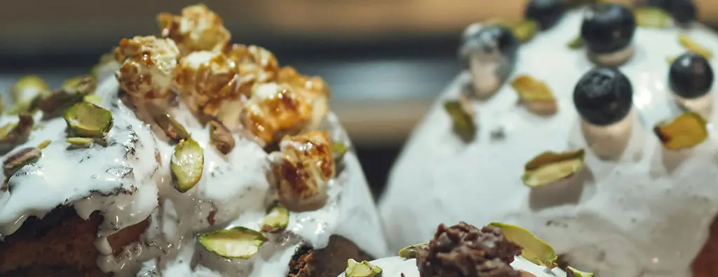 Decorated desserts feature creamy white icing topped with popcorn, blueberries, and pistachios. The rich textures and colours convey a tempting and indulgent mood.