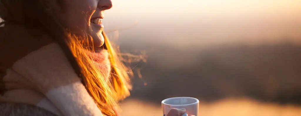Caucasian woman with a cup of coffee outdoors at sunset