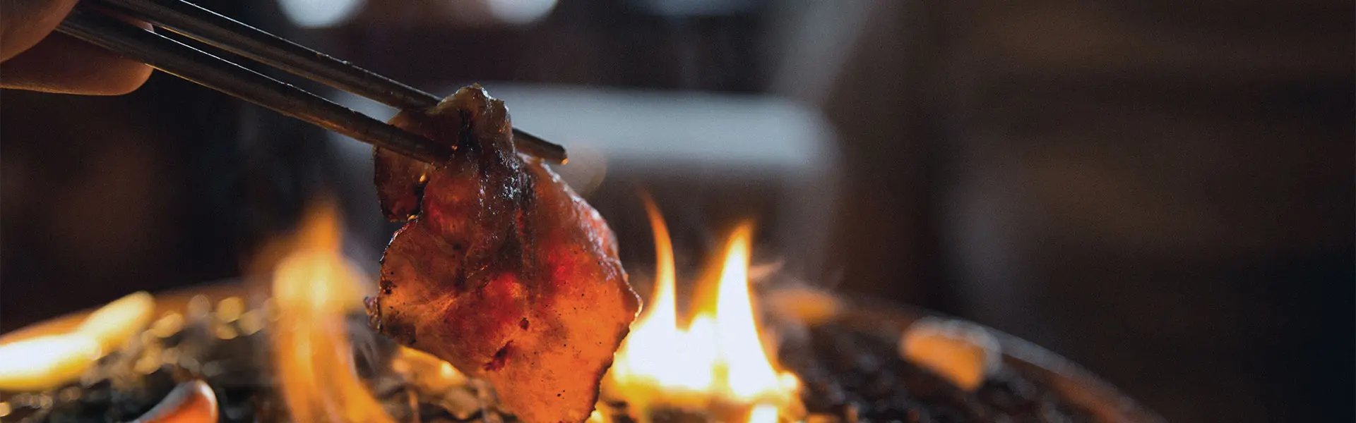 A pair of chopsticks holding meat over a grill