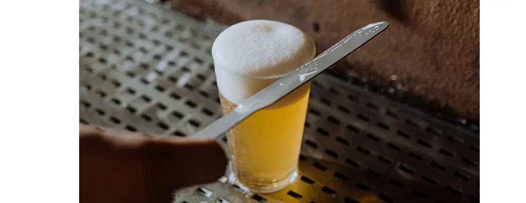 A knife over a glass of beer removing the excess foam