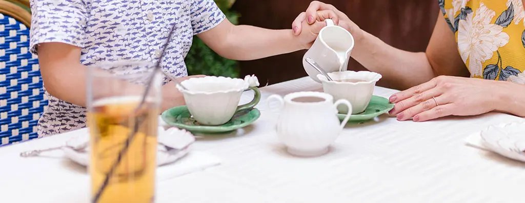Two people pooring milk in a cup of tea