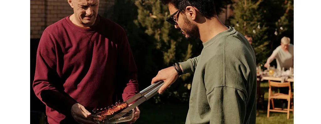 Two  men at a barbecue, one is serving grilled meat to the other