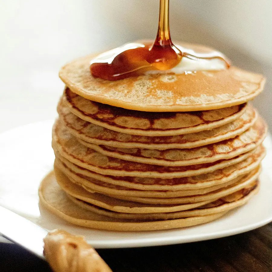 A stack of American pancakes covered with honey on a plate