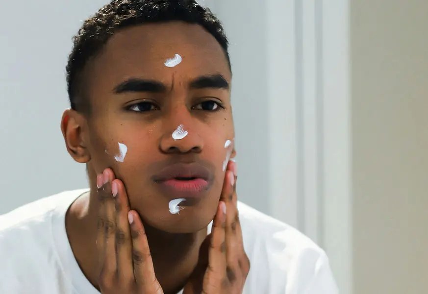Young man applying moisturiser on his face
