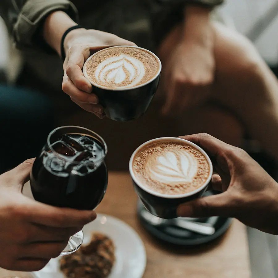 Two people each holding a cup of coffee and one holding a glass of beverage