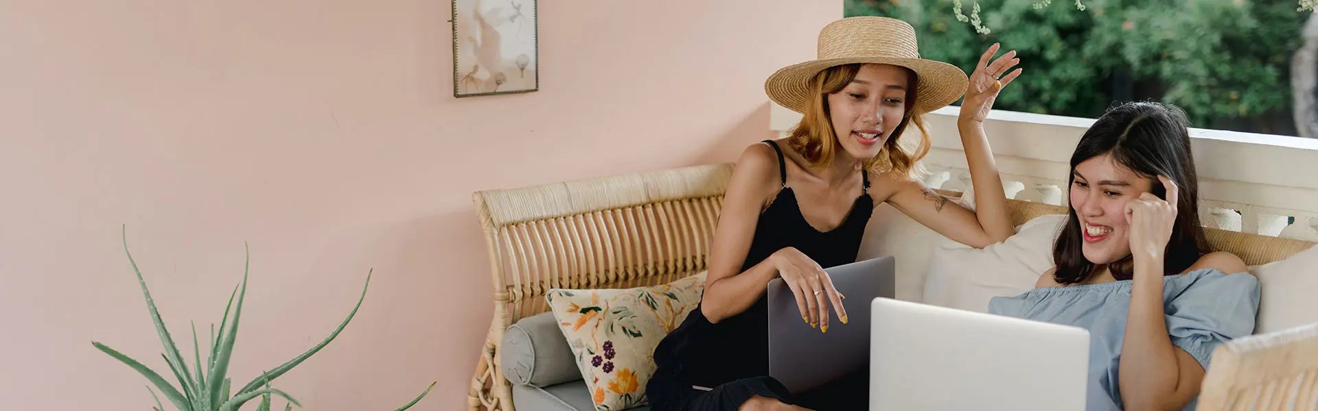 Two woman with laptops looking at one of them and smile