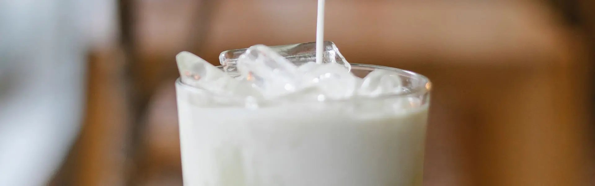 Pooring a dairy drink into a glass with ice cubes