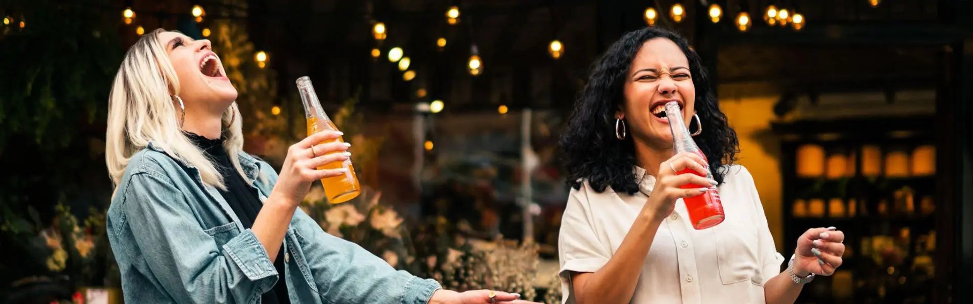 Two young woman holding coloured beverage bottles and having fun