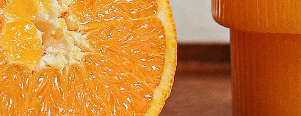 A cut orange and orange juice on a wooden serving tray on a wooden table