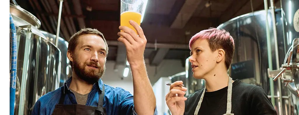 Two people looking in detail at a glass of beer