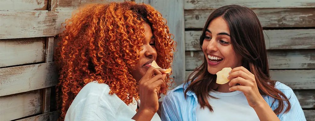 Two young women eating crisps from coloured bowls