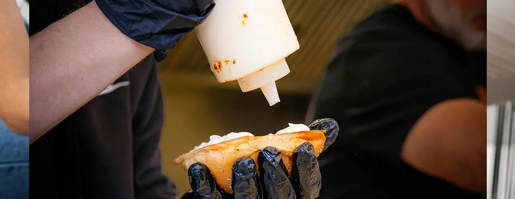 A person adding a white table sauce to a bun