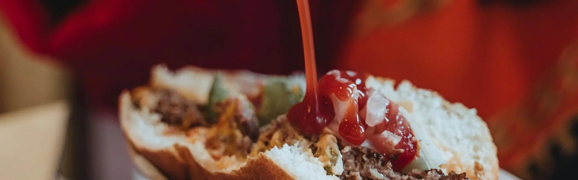Pouring tomato ketchup on a hamburger