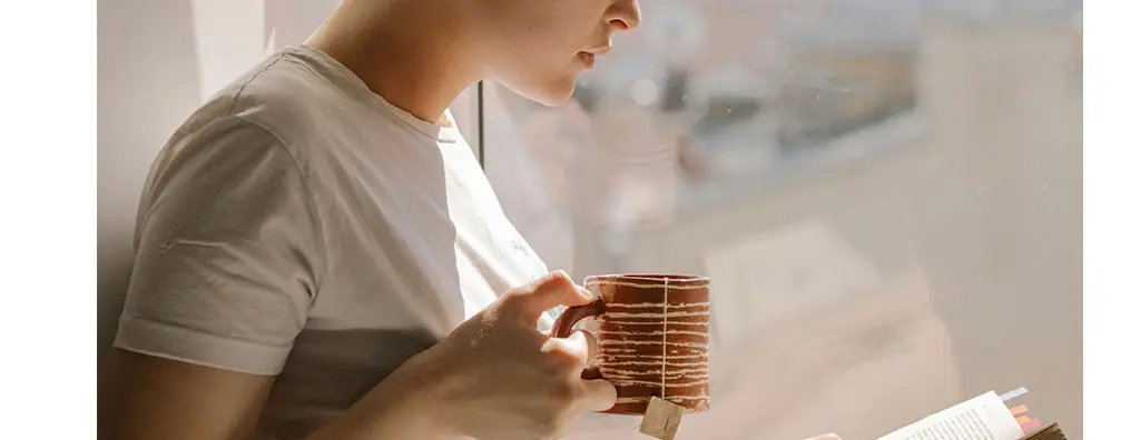 Woman reading a book while holding a mug with tea