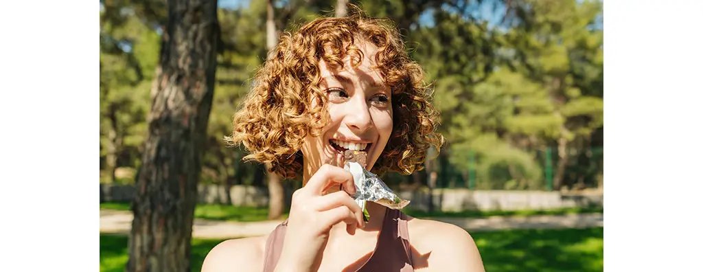 A woman eating a snack bar outdoors