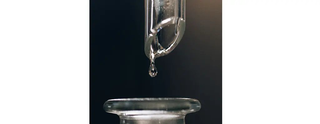 Close up of a test tube dripping liquid into a flask