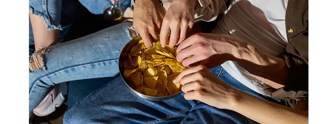 A group of people reaching for crisps in a bowl at the same time