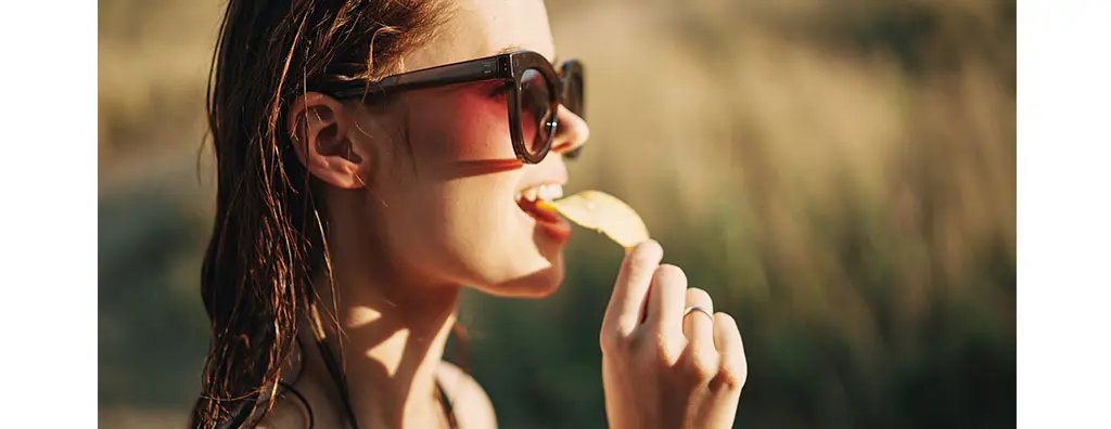A woman with sunglasses eating a crisp outdoors