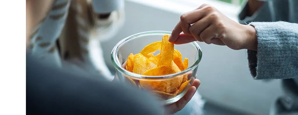 A person taking a crisp from a bowl