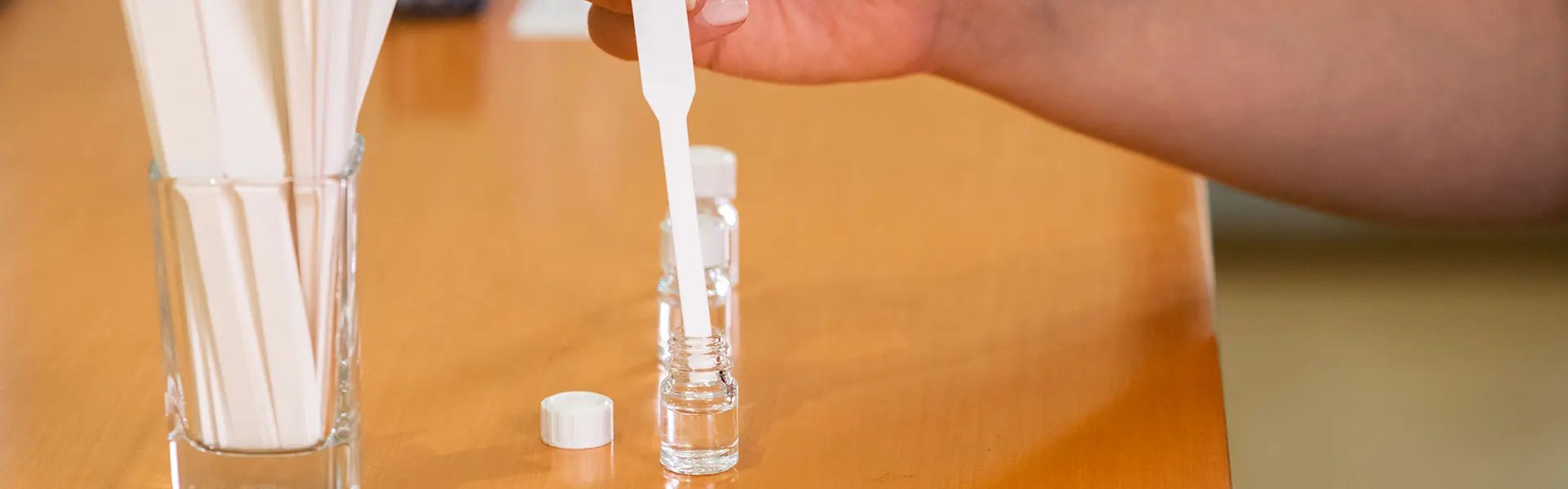 A table with glas with smelling strips and one smelling strip is dipped into some perfume