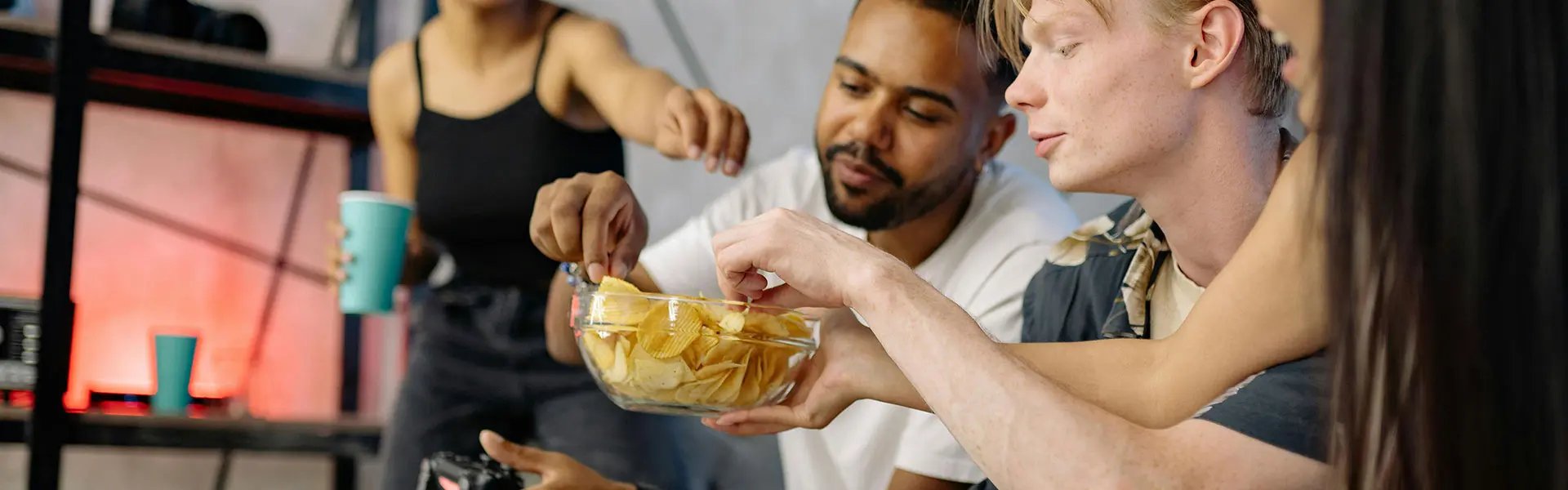 A group of people reaching out to a bowl of crisps