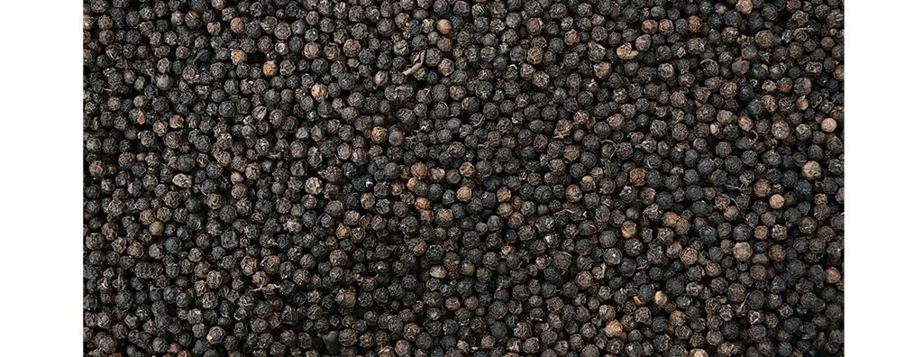 A close-up view of numerous black peppercorns, showcasing their round, textured surfaces and varying hues of dark brown and black. The overall mood suggests richness and warmth, suitable for spicing up dishes.