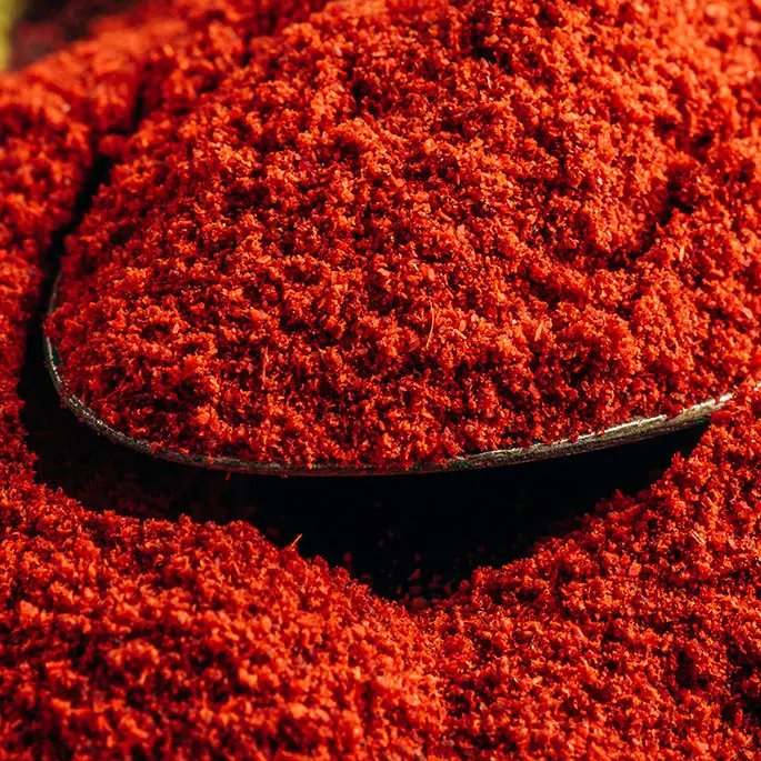 A dark red powder on a spoon representing paprika