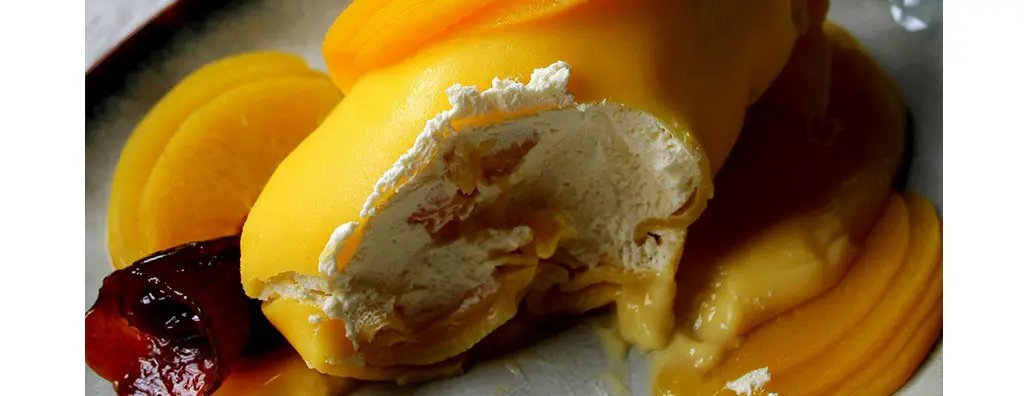 A generous serving of yellow ice cream topped with bright mango slices and a drizzle of syrup, presented on a dark ceramic plate, evokes a rich and indulgent mood.
