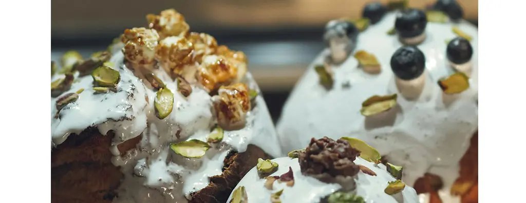 Decorated desserts feature creamy white icing topped with popcorn, blueberries, and pistachios. The rich textures and colours convey a tempting and indulgent mood.