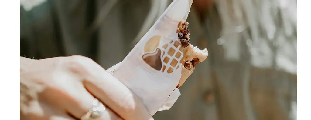A person holds a partially eaten snack bar in a decorative wrapper, with sunlight illuminating their surroundings. 