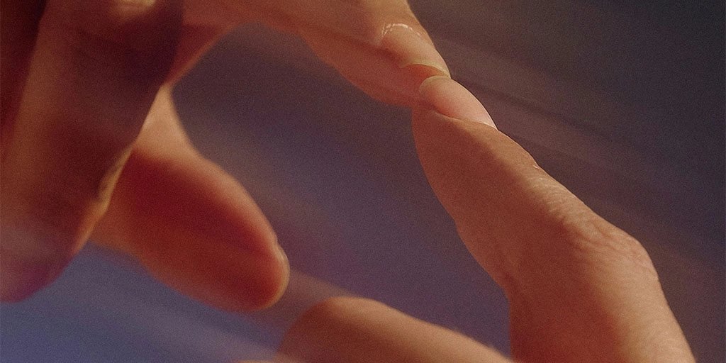 Close-up of fingers touching a mirror against a softly blurred blue and warm-toned background.