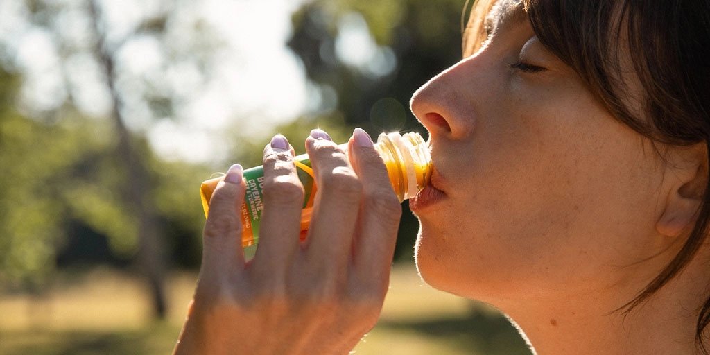 Close-up of a woman drinking an orange drink, eyes closed in warm sunlight, conveying refreshment and calm.