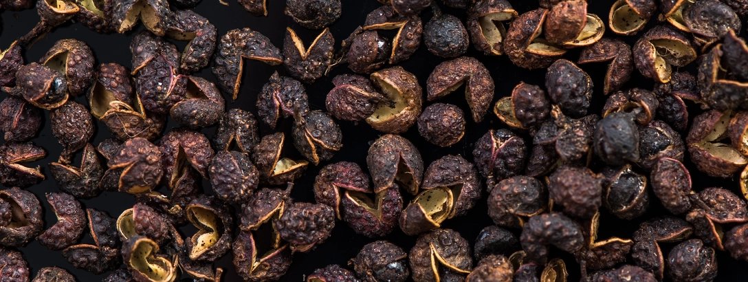 Close-up overhead view of peppercorns scattered densely across the frame, creating a rich, earthy, textured pattern.