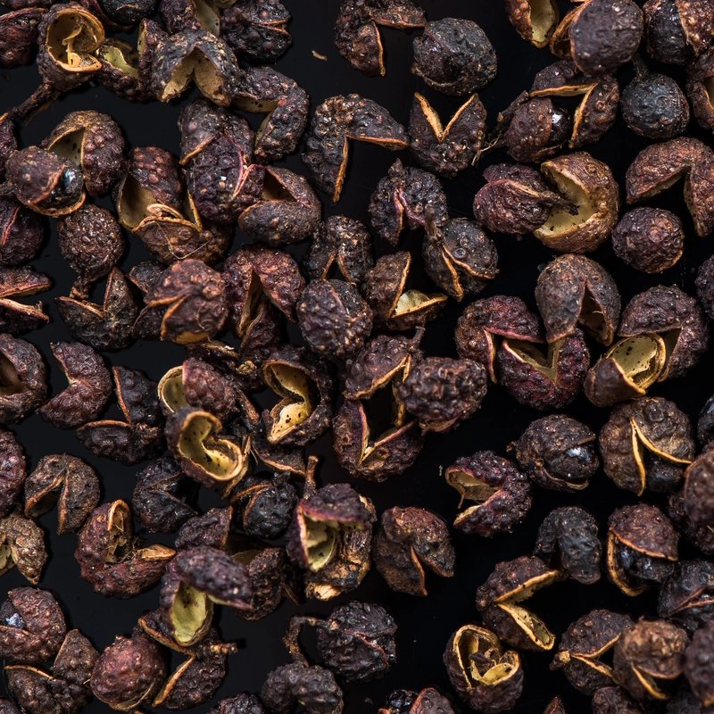 Close-up overhead view of peppercorns scattered densely across the frame, creating a rich, earthy, textured pattern.