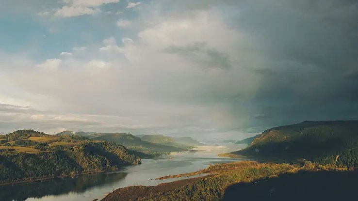 A serene landscape featuring a winding river surrounded by lush green hills under a cloudy sky. 
